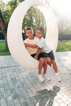 Two children sit together on a circle-shaped swing in a park during the Stock Photos