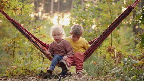 Two children sit together in a hammock in the forest Stock Footage 292132306
