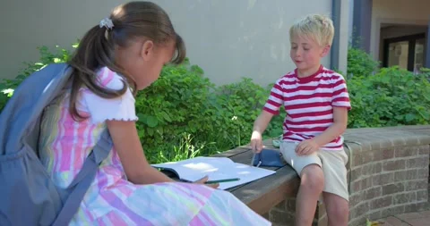 Two children sitting in courtyard, boy approaching and writing in notebook, Stock Footage 340010884