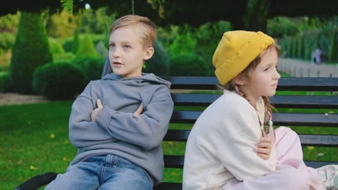 Two children sitting on a park bench with expressions of discontent as they face Stock Footage 305417130
