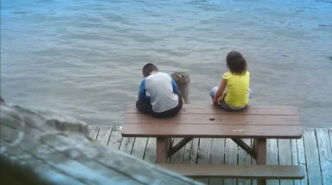Two Children Sitting on Picnic Table by Water Video stock 11106634