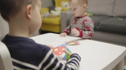 Two children sitting at table happily cutting colorful paper crafts with Stock Footage 268341017