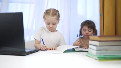 Two children sitting at table with laptop. Group of children are doing remote Video stock 317714598