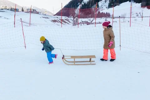 Two children in ski pants pulling the wooden sledge on snow slope Stock Photos