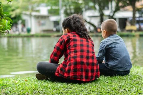 Two children on their backs looking at a lake in the park Stock Photos