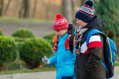 Two children walk in the park in warm clothes with backpacks on a cold autumn Stock Photos