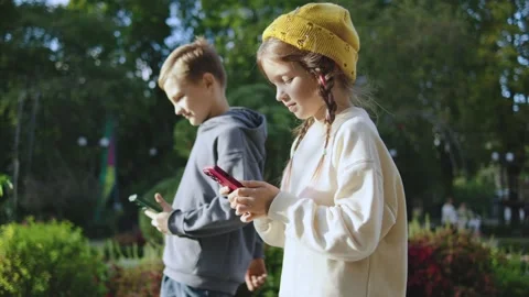 Two children walking in a park while focusing on their smartphones during a Stock-Footage 305418052
