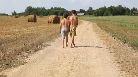 Two children  without t-shirts  walking on a sandy rural village road Stock Footage 231797935