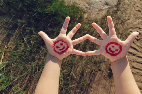 Two children's hands with red smiling faces against background of grass ans s Stock Photos