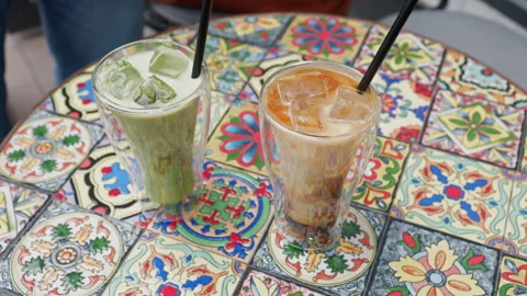 Two chilled drinks in clear glasses with black straws on colorful mosaic table Stock Footage 337648394
