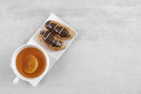 Two chocolate eclairs with cup of black tea on stone background Stock Photos