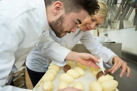 Two chocolatier apprentice decorating egg chocolate Stock Photos