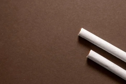 Two cigarette end laying flat on a brown background. Left area empty for copy Stock Photos