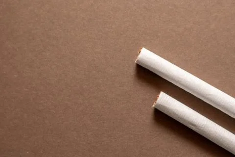 Two cigarette end laying flat on a brown background. Left area empty for copy Stock Photos