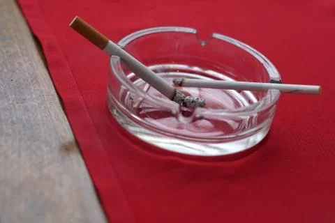 Two cigarettes of different thickness burning on the ashtray Stock Photos