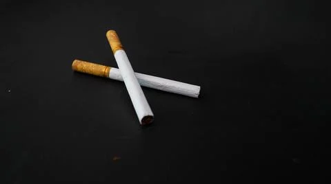 Two cigarettes placed on a black surface, highlighting the contrast between.. Stock Photos