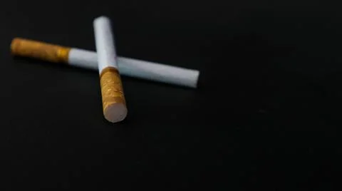 Two cigarettes placed on a black surface, highlighting the contrast between.. Stock Photos
