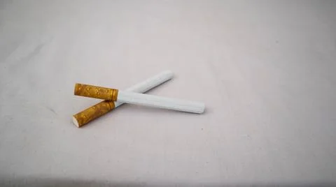 Two cigarettes placed on a white surface, showcasing their brown filters an.. Stock Photos