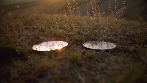 Two circle shaped mirrors laying on a field in the sunset Stock Footage 122807868
