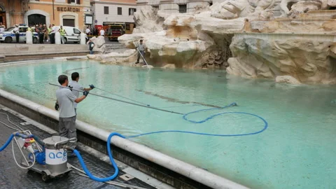 Two city workers clean coins from Trevi Fountain and police cars in the Stock Footage 156238342
