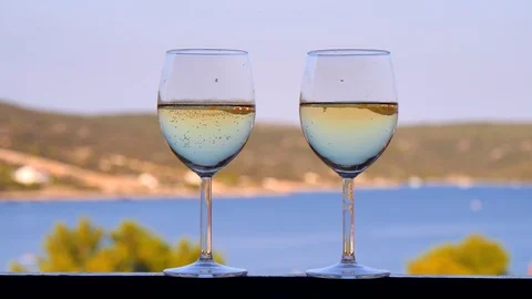 Two classic glasses of white wine close-up stand on the background of the sea Stock Footage 124702282