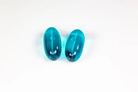 Two clear blue pills against the while surface of a pharmacy table. Stock Photos