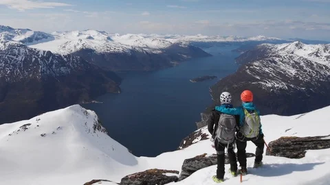 Two climbers hug on a mountain overlooking a fjord in Norway aerial Stock Footage 99738365