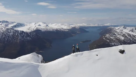 Two climbers on mountain ridge overlooking a fjord Norway aerial view Stock Footage 99738332