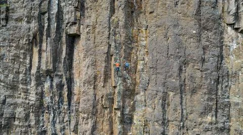 Two climbers practicing mountaineering on vertical stone wall Stock Photos