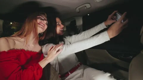 Two close girlfriends are joyfully taking a selfie while sitting in their car Stock Footage 298265214