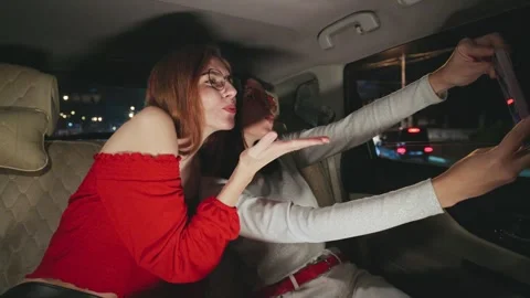 Two close girlfriends are joyfully taking a selfie while sitting in their car Stock Footage 298265861
