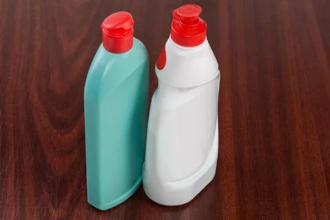 Two closed plastic bottles of cleaning agent on wooden surface Stock Photos
