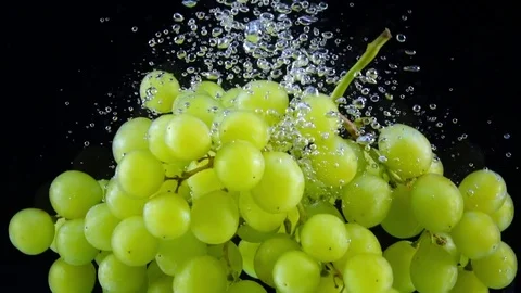 Two clusters of juicy green grape dropping into the water in slow motion. Vídeo Stock 77002525