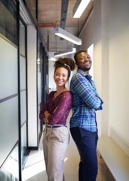 Two co-founders stand back to back with arms crossed in office corridor Stock Photos