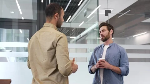 Two co-workers engaging in casual discussion while standing in modern office.  Stock Footage 309644186