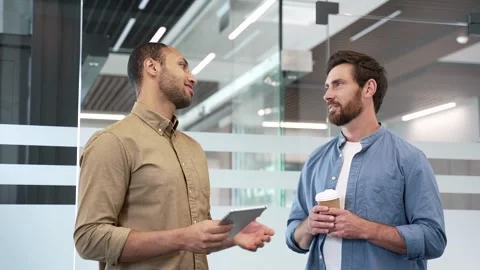 Two co-workers engaging in casual discussion while standing in modern office.  Vídeos de archivo 338060582