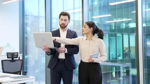 Two co-workers, man and woman engaged in discussion holding a laptop in office.  Stock Footage 298996942