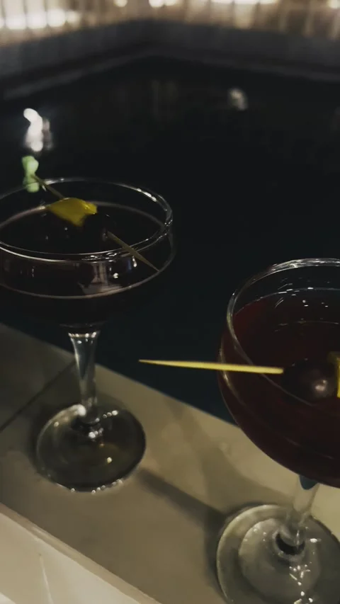 Two cocktail glasses with fruit garnish near an indoor pool Stock Footage 345145803
