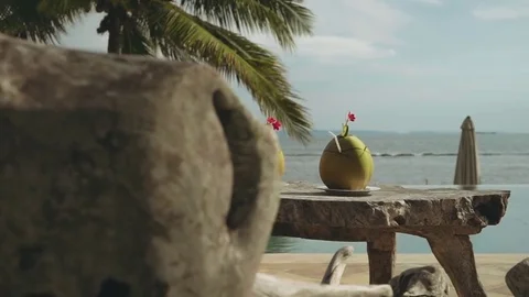 Two coconut drinks on wooden table in front of infinity swimming pool and ocean Stock Footage 77862317