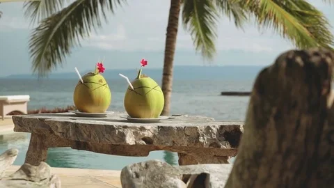 Two coconut drinks on wooden table in front of infinity swimming pool and ocean Stock-Footage 77862323