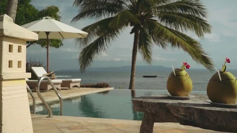 Two coconut drinks on wooden table in front of infinity swimming pool and ocean Stock Footage 77862327