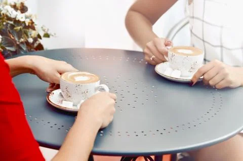 Two coffee cups and hands of young women at outdoor cafe Stock Photos
