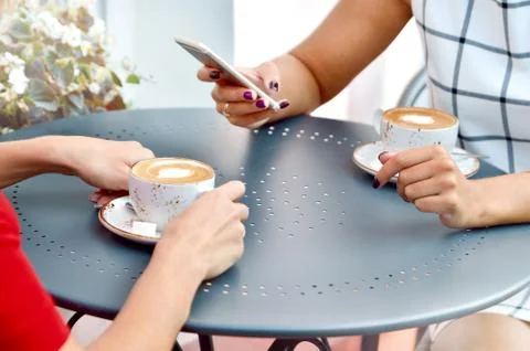 Two coffee cups and hands of young women with smartphone at outdoor cafe Stock Photos