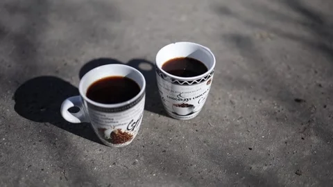 Two coffee cups rest on the pavement, casting deep shadows under the bright sunl Video stock 304623161