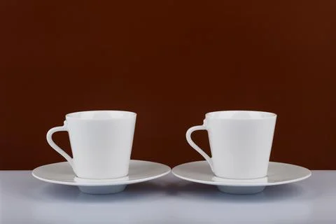 Two coffee cups on white table against brown background with space for text Stock Photos