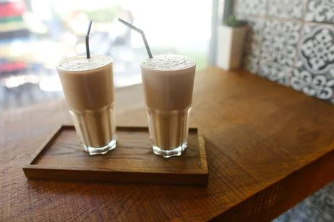 Two coffee drinks in in glass cup with drinking straw stand on table in coffee Stock Photos