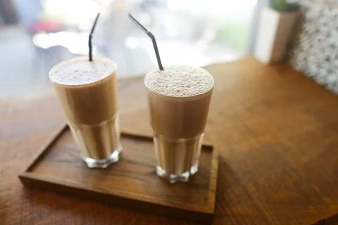 Two coffee drinks in in glass cup with drinking straw stand on table in coffee Stock Photos
