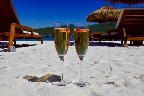 Two cold glasses of champagne with raspberry on white sand on the beach in an 库存照片