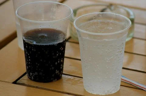 Two cold soft drink plastic glasses - black and colorless drinks Stock Photos