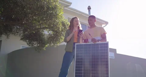 Two collaborators checking mobile device, pointing to solar panel front of house Stock Footage 342018788